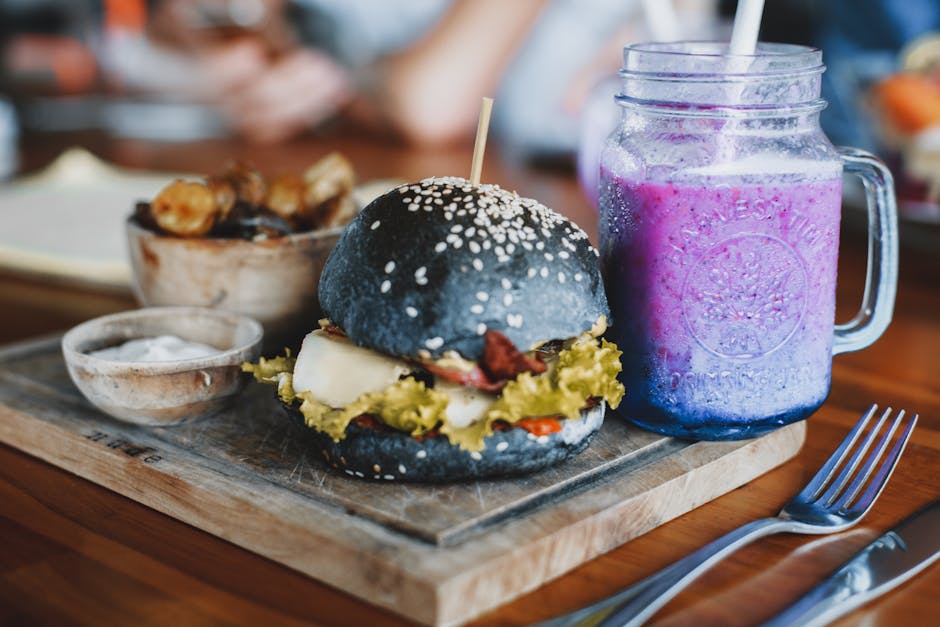 A gourmet black bun burger served with a vibrant berry smoothie in a café setting